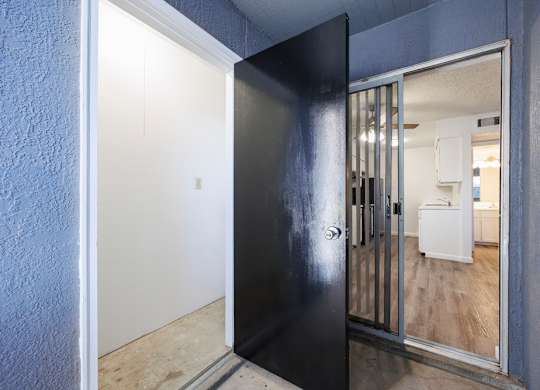 A black door with a glass window is open to a room with a white fridge.