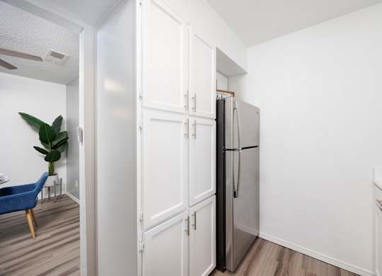 A kitchen with a refrigerator, a chair, and a plant.