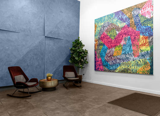 A colorful abstract painting hangs on a wall next to two chairs and a small table.