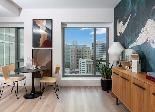 A modern living room with a table, chairs, and a large window overlooking the city.