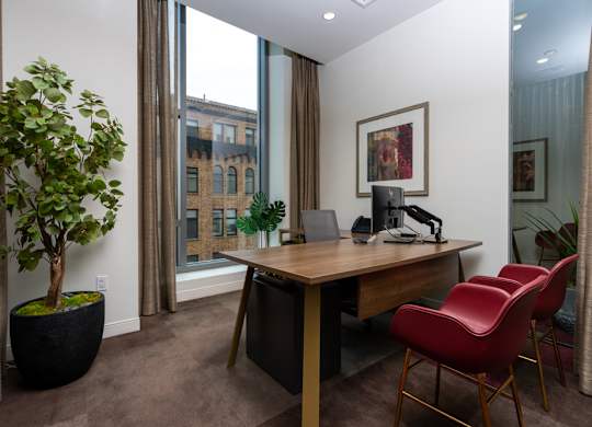 A room with a desk, chair, and potted plant.