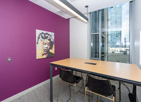 A purple wall with a poster and a table with chairs.