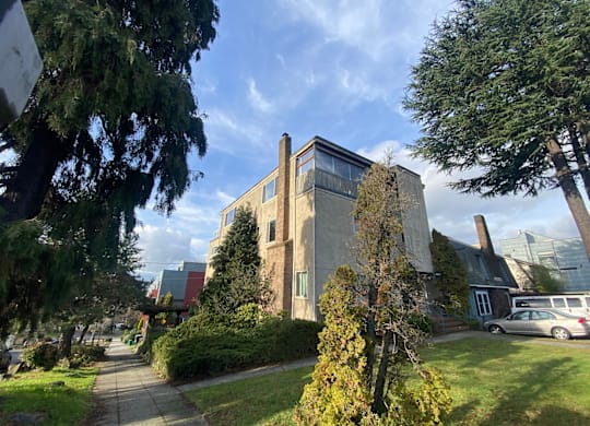 A large building with a flat roof and a chimney is surrounded by trees and bushes.