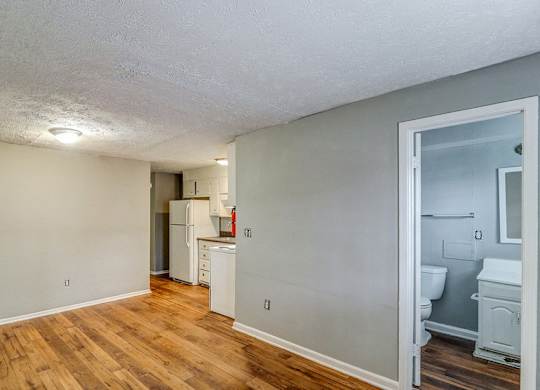 A room with wooden floors and a white ceiling with a kitchen area visible through the door.at Waverly Manor Townhomes, Norcross, 30071  