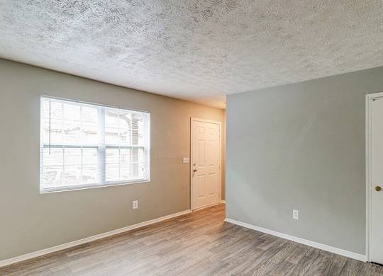 A room with a window, two doors, and a wooden floor.at Waverly Manor Townhomes, Georgia  