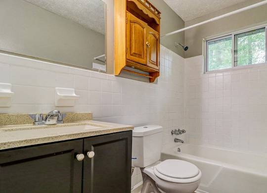 A white toilet sits in a bathroom with a white tub and a window.at Waverly Manor Townhomes, Norcross, GA  