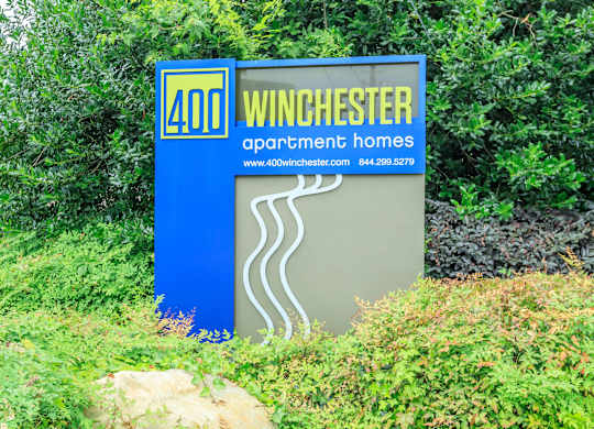 A blue and white sign for Winchester Apartment Homes sits in front of some greenery.