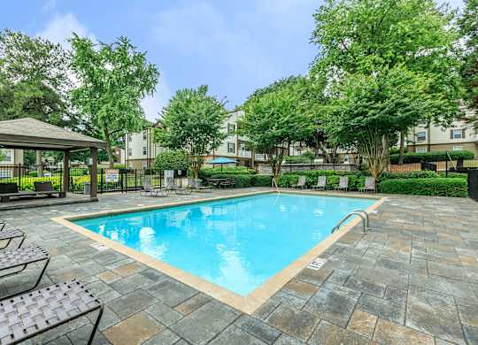 A pool surrounded by trees and a patio area.