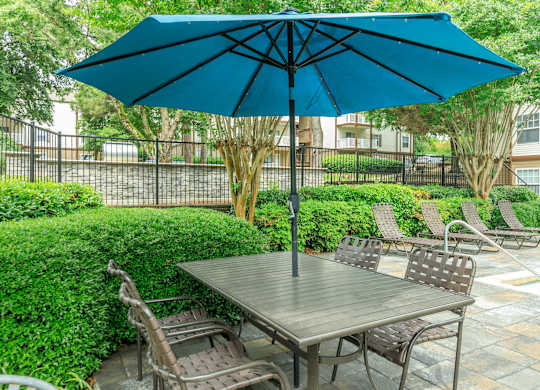 A blue umbrella shades a table and chairs in a backyard.