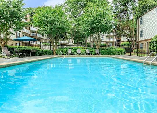 A swimming pool surrounded by trees and apartment buildings.