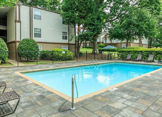A small pool surrounded by a stone patio and a black fence.