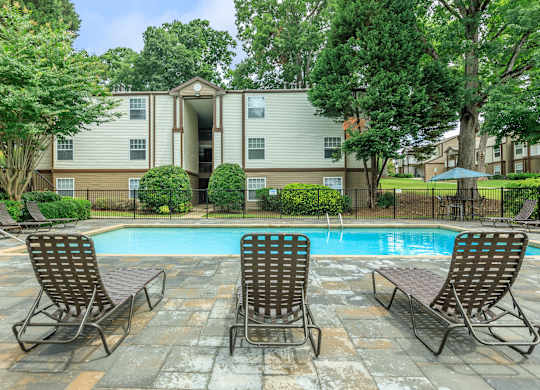 A pool surrounded by chairs and trees in front of a building.