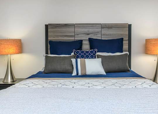 A bed with a white comforter and blue pillows is flanked by two lamps.
