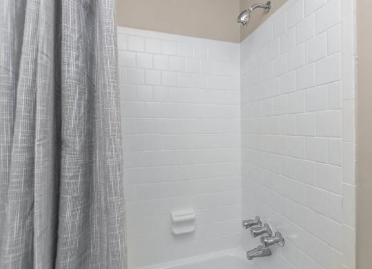 A white tiled shower with a grey curtain.