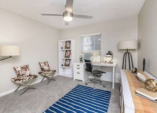 A room with a desk, chairs, and a ceiling fan.
