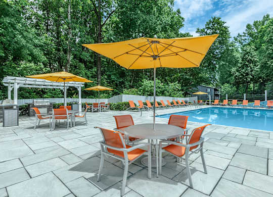 A poolside table with chairs and umbrellas is set up next to a pool at Crest at East Cobb Apartments, Marietta