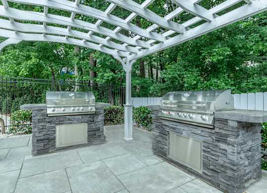 A patio with two grills under a white pergola at Crest at East Cobb Apartments, GA, 30062