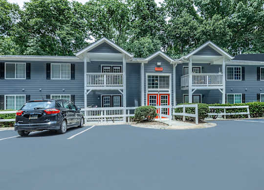 A car is parked in front of a grey building with a red door at Crest at East Cobb Apartments, Marietta