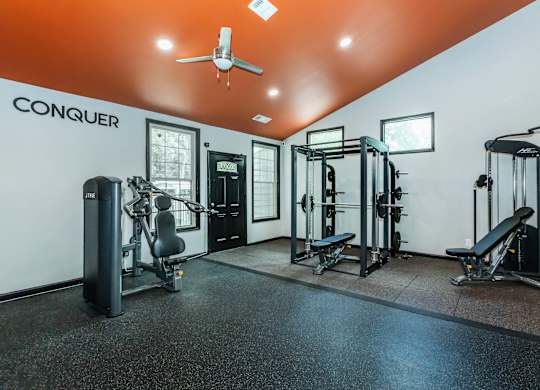 A gym with a variety of equipment including a weight bench, a leg press machine, a squat rack, and a treadmill at Crest at East Cobb Apartments, Marietta