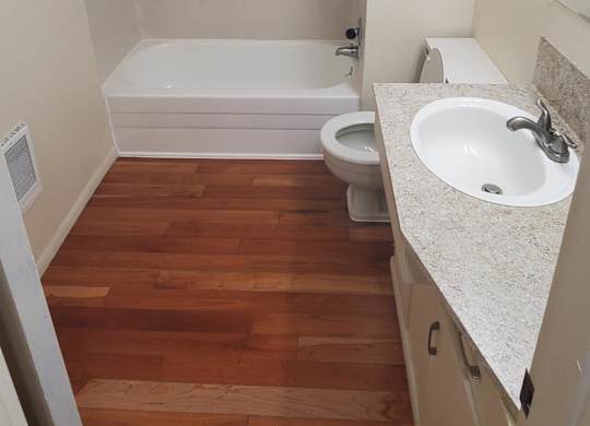 A white bathroom with a wooden floor and a white tub.