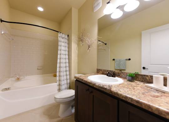 A bathroom with a white toilet, a bathtub with a shower curtain, and a sink with a mirror above it at Cabana Club - Galleria Club Apartments, Florida