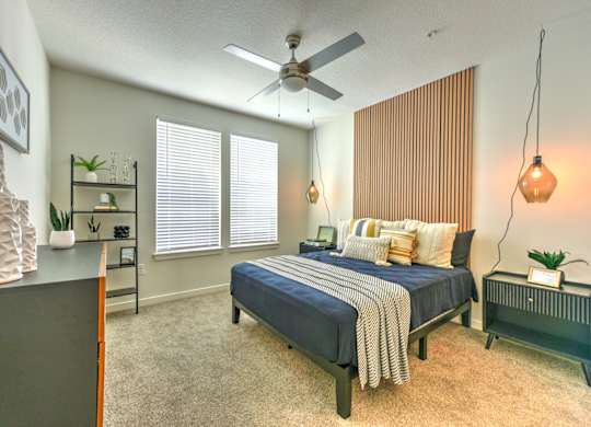 A bedroom with a bed, a ceiling fan, and a nightstand with a lamp at Fusion Apartments, Jacksonville, FL