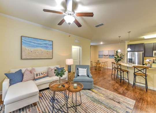 A living room with a white couch and a painting of a beach scene on the wall at Cabana Club - Galleria Club Apartments, Florida 32256