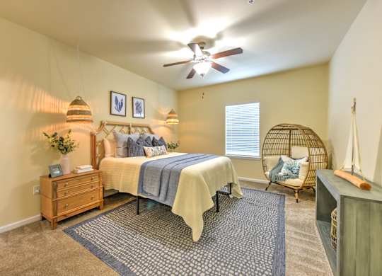 A bedroom with a bed, a chair, and a ceiling fan at Cabana Club - Galleria Club Apartments, Florida 32256
