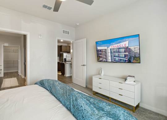 A bedroom with a bed, dresser, and a painting of a building on the wallat Pinnacle Apartments, Jacksonville, FL