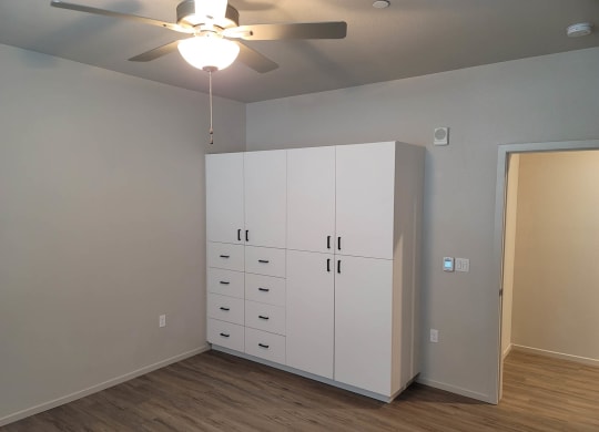 White cabinet built in wardrobe in bedroom with ceiling fan and wood flooring.
