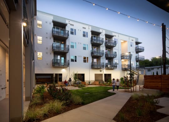 Interior courtyard at dusk with lighted balconies and walkways, showing green courtyard and walking path.