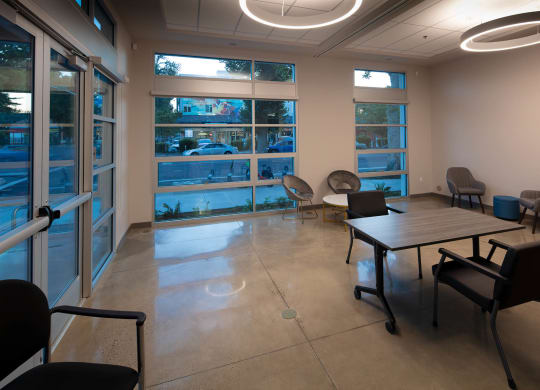 Open space and small meeting room in community room with large windows facing street, tables, and chairs.
