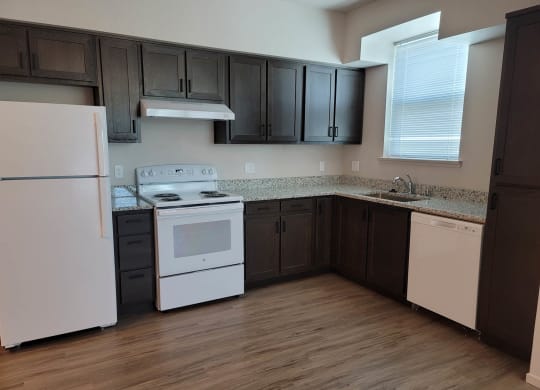 Kitchen with dark wood cabinets and white appliances, window over sink.