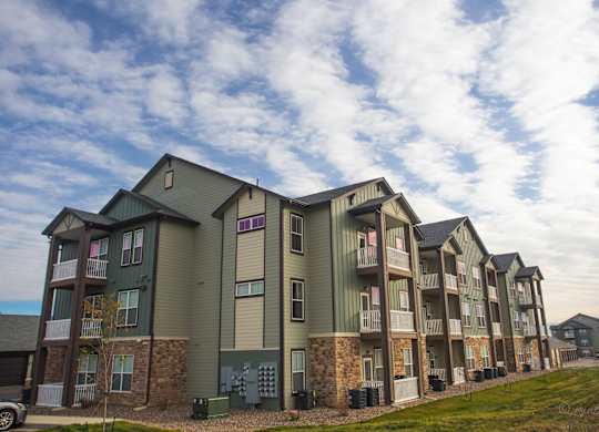 Apartment complex with green and brown buildings and a cloudy sky.