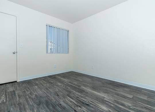A room with a wooden floor and a window with blinds.