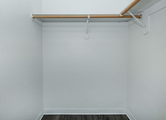 A white wall with a shelf and a wooden floor.