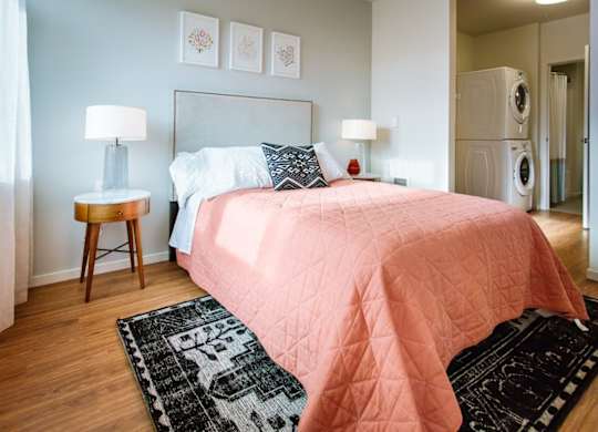 A bedroom with a pink bedspread and a black and white rug.