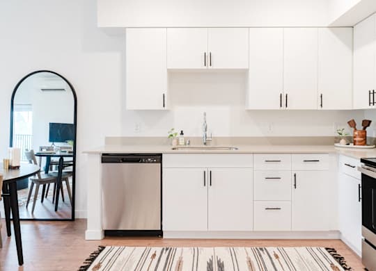 A modern kitchen with white cabinets and a striped rug on the floor.