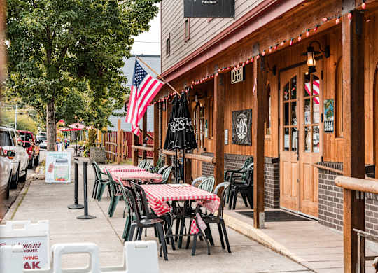 A restaurant with tables and chairs outside with an American flag hanging on the wall.