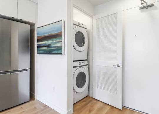 A white laundry room with a refrigerator, a washer and a dryer.