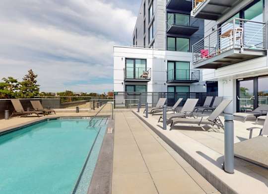 A swimming pool is surrounded by lounge chairs on a patio.