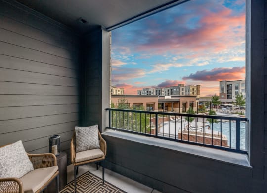 a balcony with two chairs and a view of a city at sunset