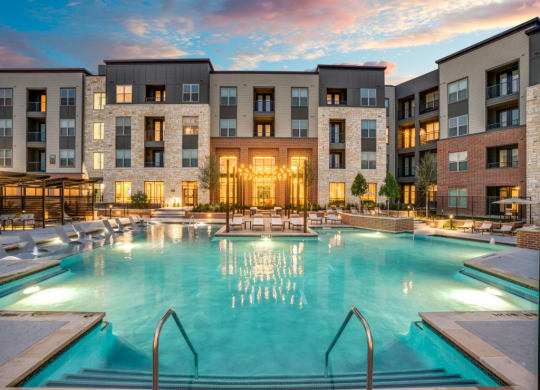 a swimming pool in front of an apartment building at sunset