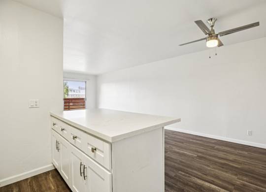 A white kitchen with a ceiling fan and wooden flooring.