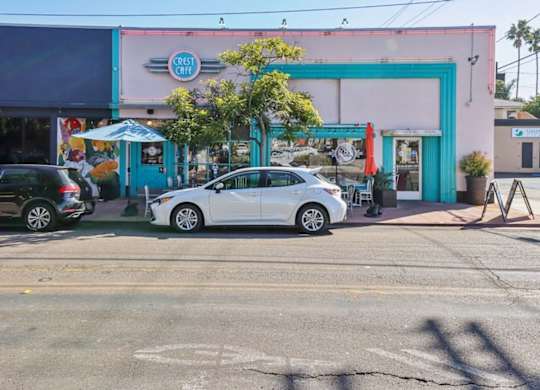 A white car is parked in front of a pink building with a blue door.