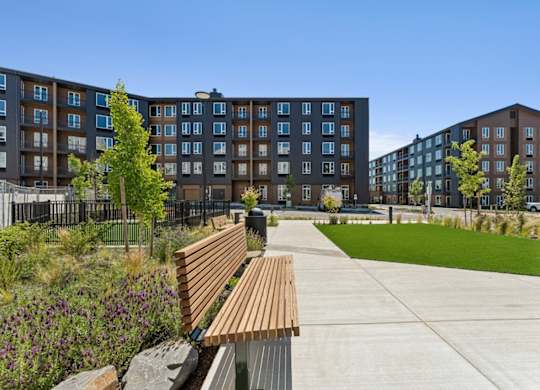 A wooden bench sits on a concrete path in front of apartment buildings.