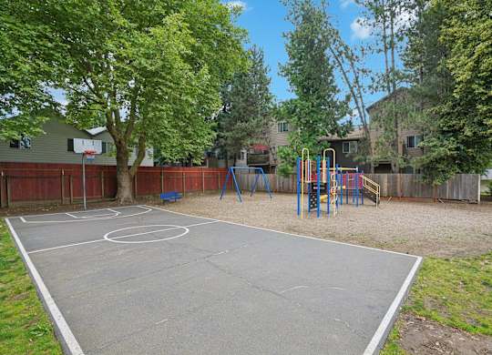 A basketball court is surrounded by a fence and trees.