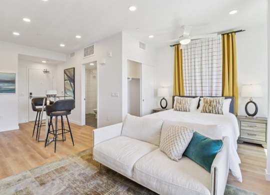 A white couch with blue and white pillows sits in a living room with a bar area and a dining area in the background.