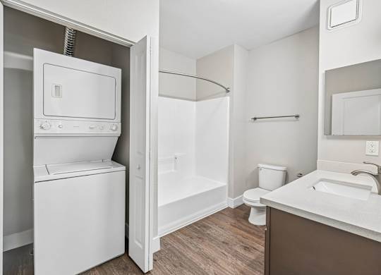 A white washing machine is in a small bathroom with a toilet and sink.