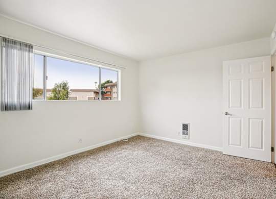 A room with a white door and a window with a view of buildings outside.